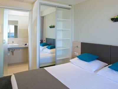 Moderner Hotelraum mit Doppelbett, blauen Kissen und angrenzendem Badezimmer.
