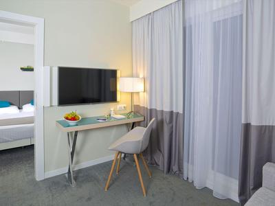 Moderner Hotelraum mit Schreibtisch, Stuhl, Fernseher und angrenzendem Schlafzimmer.