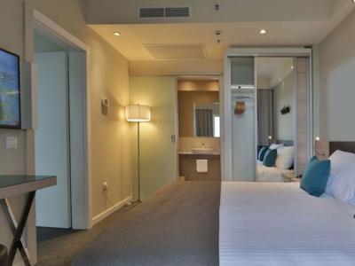 Modernes Hotelzimmer mit Doppelbett, Glas-Tisch und offenem Badezimmerbereich.