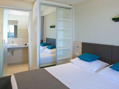 Modernes Hotelzimmer mit Doppelbett, grauer Bettdecke und Zugang zum Badezimmer.