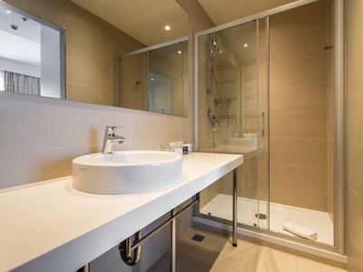 Modernes Hotelbadezimmer mit Glasdusche, rundem Waschbecken und großem Spiegel.