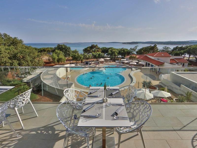 Balkon z miejscami do siedzenia z widokiem na basen, drzewa i morze w hotelu.