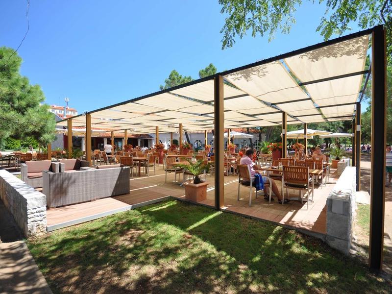 Duży zadaszony taras z miejscami do siedzenia pod czystym niebem i drzewami w tle.