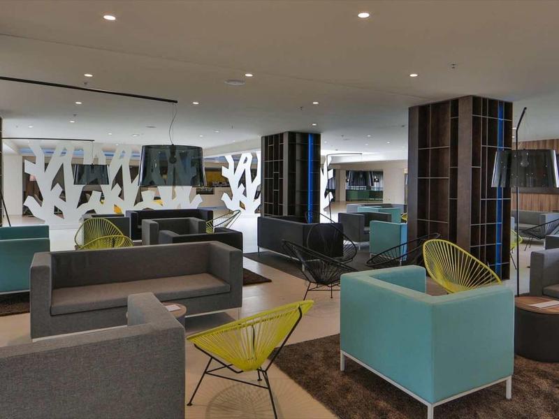 Nowoczesna poczekalnia hotelowa z kolorowymi siedziskami i dużymi oknami.