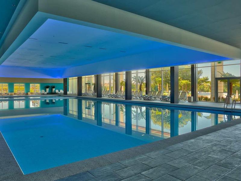 Nowoczesny kryty basen z dużymi oknami i niebieskim oświetleniem w hotelu.