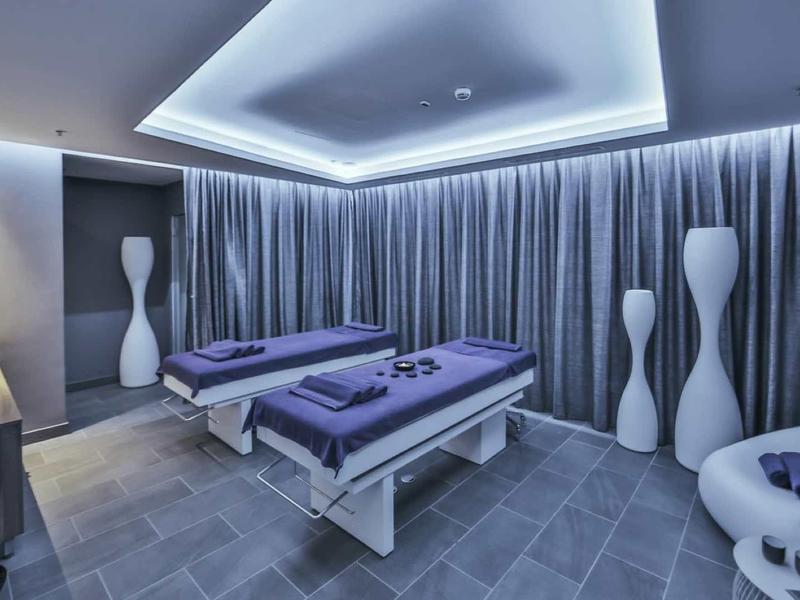 Nowoczesny pokój spa z dwoma stołami do masażu, miękkim oświetleniem i zasłonami.