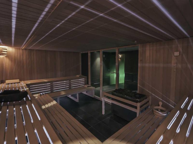 Pomieszczenie sauny z drewnianymi panelami i ławkami, przyciemnione oświetlenie, nowoczesny wygląd.