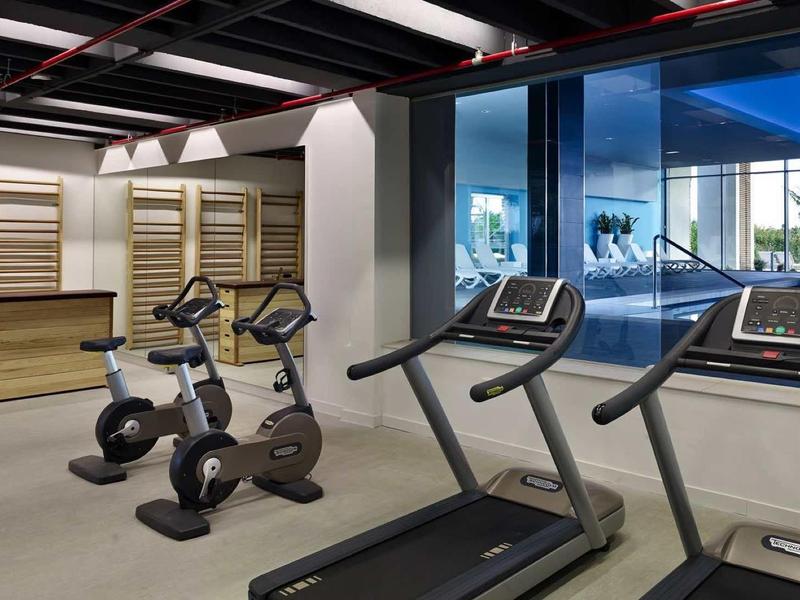 Nowoczesna siłownia z dwoma bieżniami, dwoma rowerkami stacjonarnymi i dużym oknem.