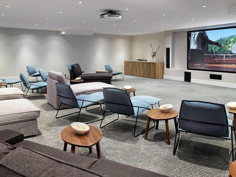 Nowoczesna sala konferencyjna z wygodnymi krzesłami, stolikami i dużym ekranem na ścianie.