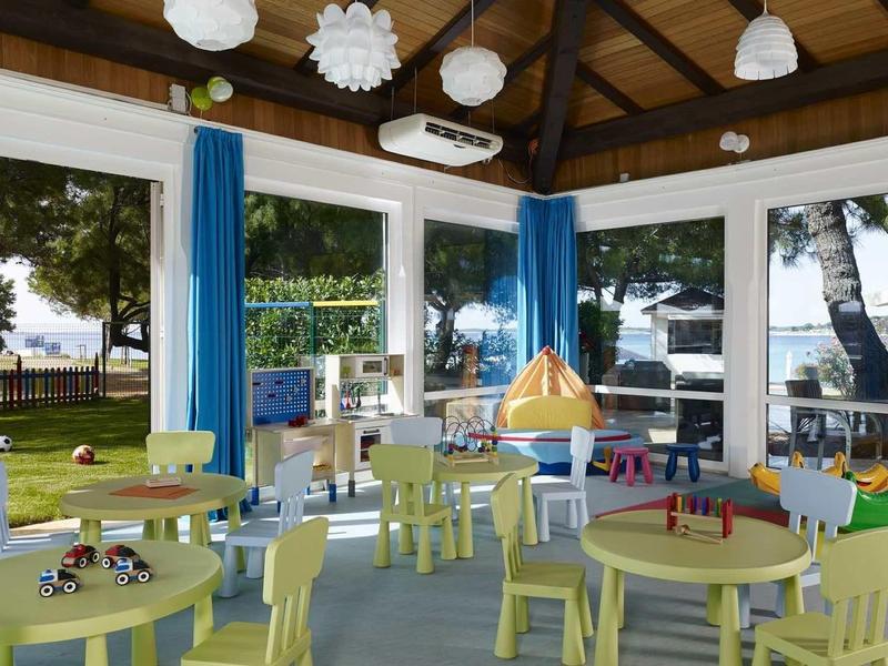 Kolorowy, jasny kącik zabaw dla dzieci z stolikami, krzesłami i dużymi oknami w ośrodku wypoczynkowym.