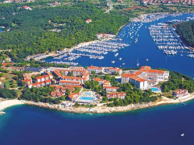 Zdjęcie lotnicze nadmorskiego miasta z mariną i plażami, otoczone zielenią.