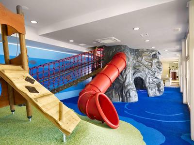 Sala zabaw zjeżdżalnią, mostkiem i strukturą do wspinaczki w jaskrawych niebieskich i czerwonych kolorach.