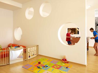 Jasny pokój zabaw dla dzieci z wyściełaną podłogą i zabawkami obok otwartej kuchni.