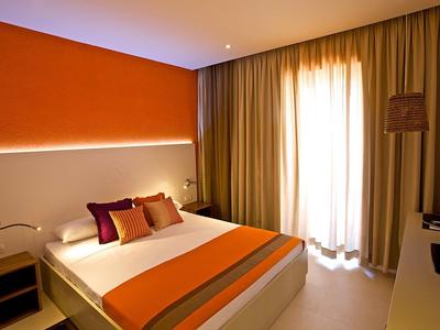 Nowoczesny pokój hotelowy z dużym łóżkiem, pomarańczową ścianą i zasłonami.