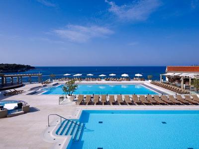 Luksusowy basen z leżakami, parasolami i widokiem na morze w słoneczny dzień.