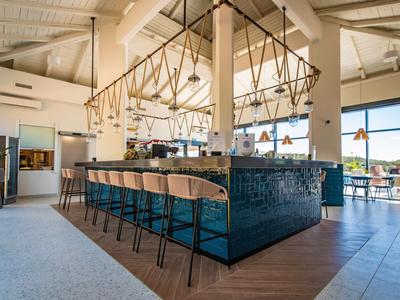 Nowoczesny bar hotelowy z drewnianymi stołkami, niebieskimi płytkami i dużymi oknami z widokiem.