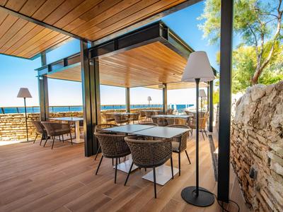 Nowoczesny odkryty obszar wypoczynkowy z stołami i krzesłami otoczony naturą i kamiennymi ścianami.