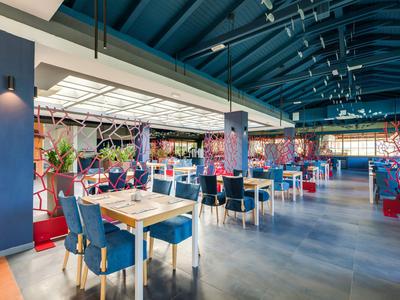 Helle, geräumige Hotellounge mit blauen Stühlen und Holztischen unter hoher Decke.