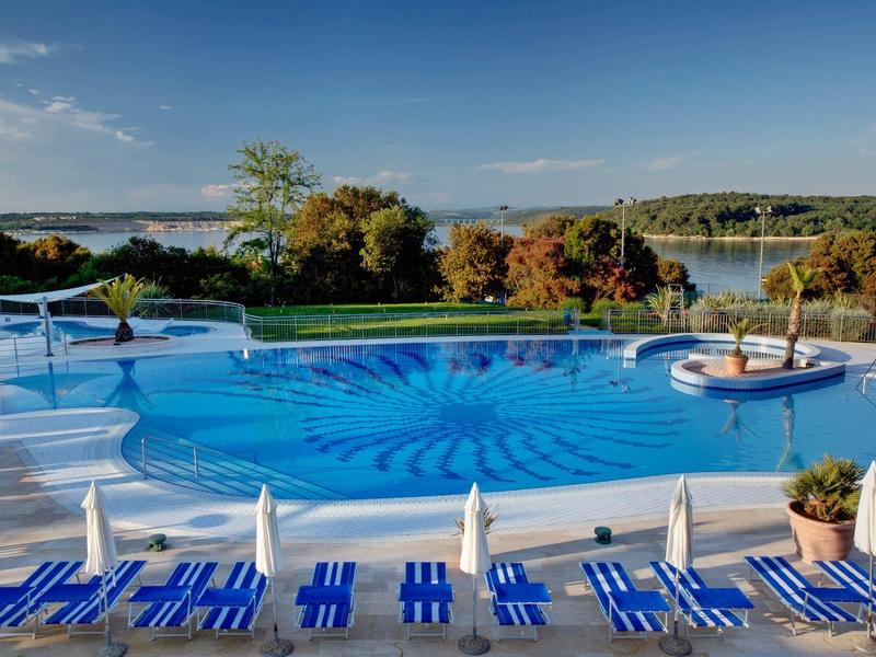 Bazén s modrobílými lehátky u jezera pod modrou oblohou.