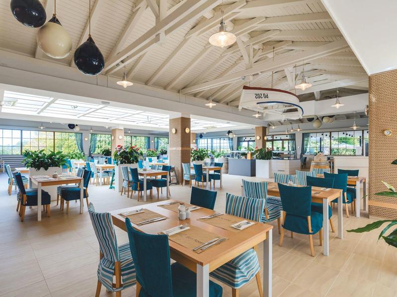 Prostorná, světlá hotelová restaurace s dřevěnými stolky a pohodlnými modrými židlemi.