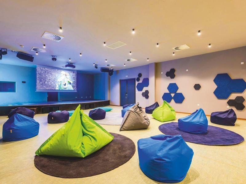 Moderní seminární místnost s barevnými sedacími vaky a velkými obrazovkami na zdech.