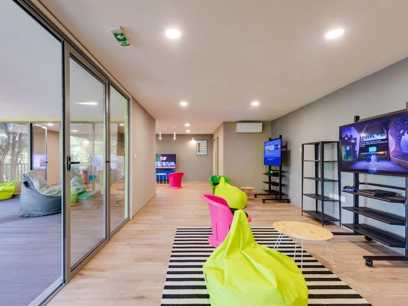 Moderní hotelová lounge s barevnými sedacími vaky a televizory na stěně.