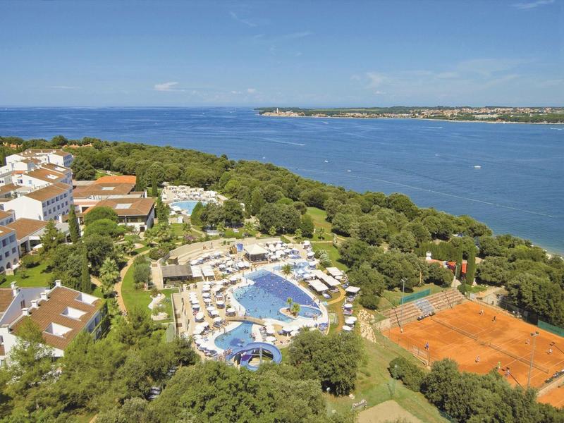 Letecký pohled na resort s bazény, tenisovým kurtem a výhledem na moře.