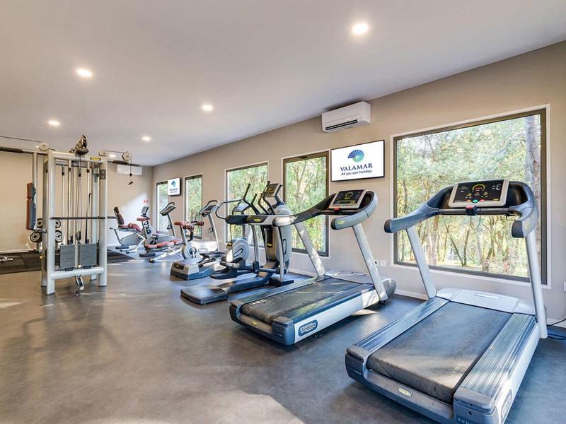 Moderní posilovna s běžeckými pásy, stacionárními koly a posilovacími stroji s velkými okny.