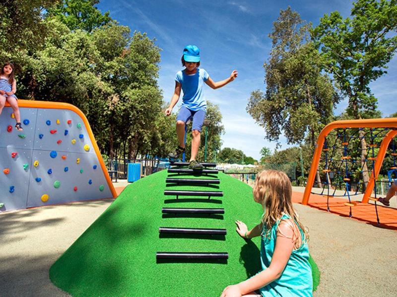Děti si hrají na venkovním hřišti s horolezeckou stěnou, skluzavkou a houpačkami