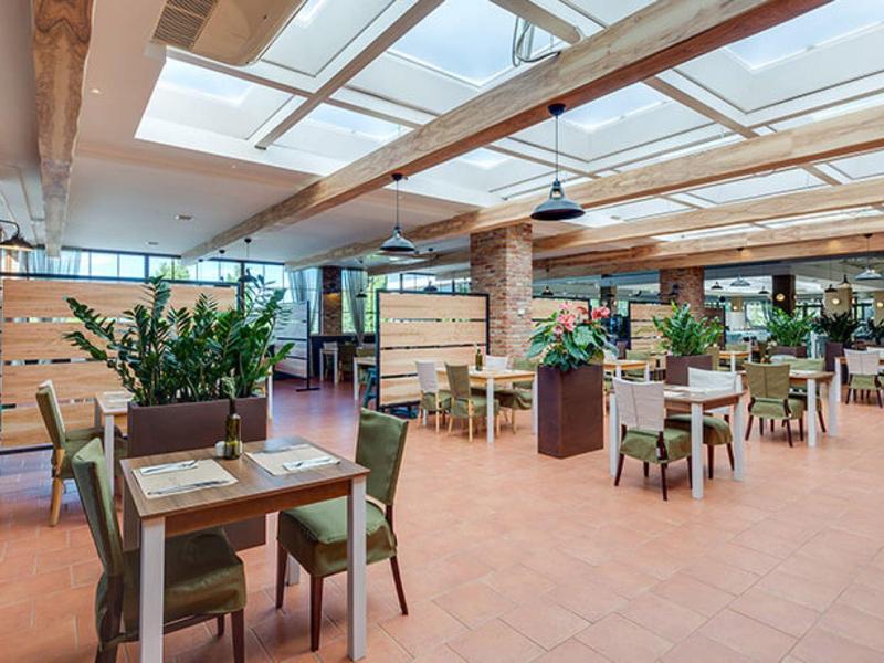 Světelná a prostorná restaurace se skleněnou střechou a moderním dřevěným nábytkem.