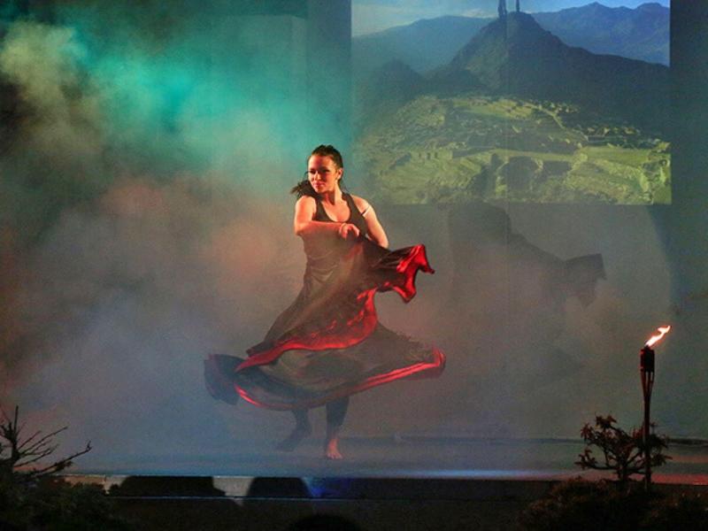 Tanečnice v červených šatech na kouřové scéně s hořícími pochodněmi.
