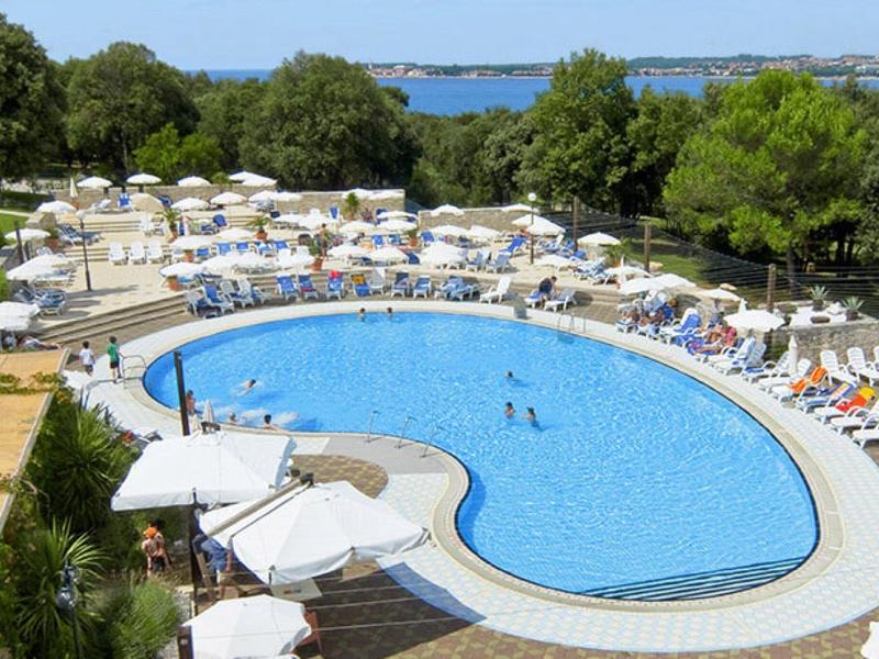 Velký venkovní bazén s deštníky a lehátky v zahradě poblíž moře.