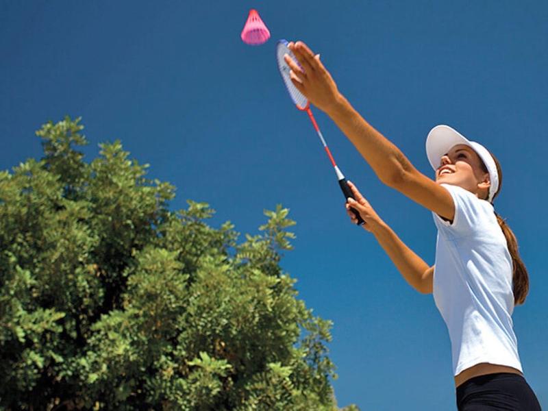 Žena hrající badminton venku pod jasnou oblohou vedle stromů.