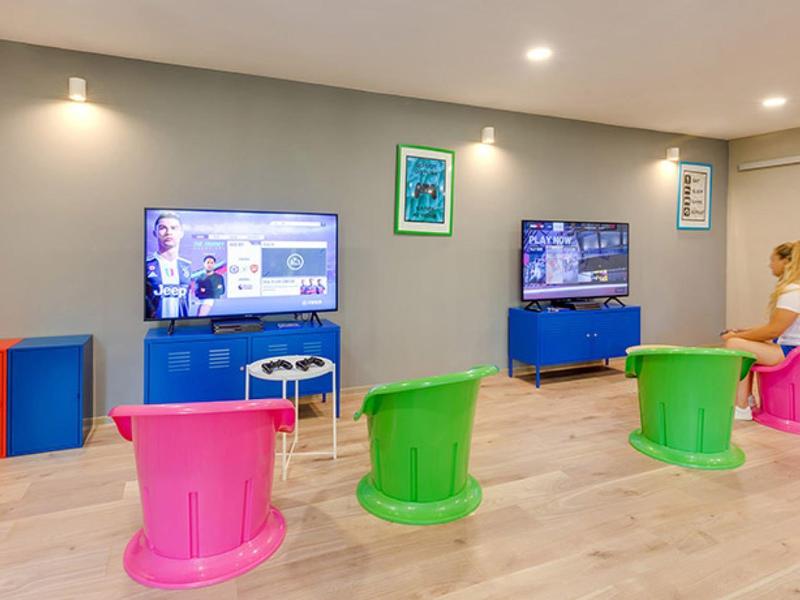 Barevná herní zóna s konzolemi a jasnými stoličkami v moderní místnosti.