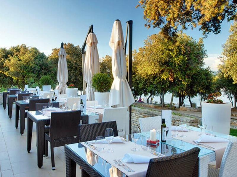 Terasa s prostřenými stoly a židlemi pod modrou oblohou a stromy.