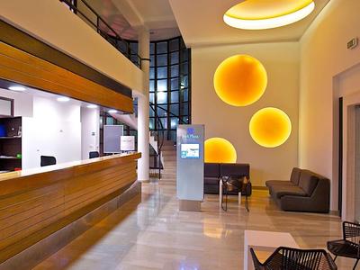 Moderní hotelová lobby s dřevěnou recepcí, posezením a kulatými osvětlenými stěnovými dekoracemi.