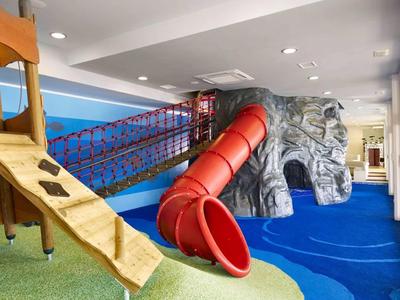 Innen-Spielplatz mit Rutsche, Klettergerüst und Kletterwand in bunten Farben und weichem Boden.