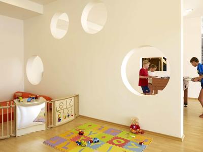 Hell gestalteter Spielbereich mit buntem Teppich, Holzspielzeug und zwei Kindern in hellem Raum.