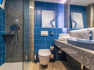 Moderner Badezimmer mit blauen Fliesen, Glasdusche, Waschbecken und weißen Handtüchern.