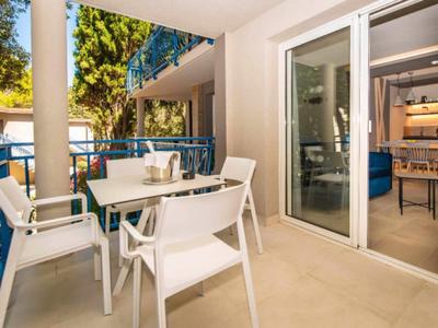 Balkon mit weißen Stühlen und Tisch, blauer Geländer, Grün und Blick ins Wohnzimmer mit Kamin.