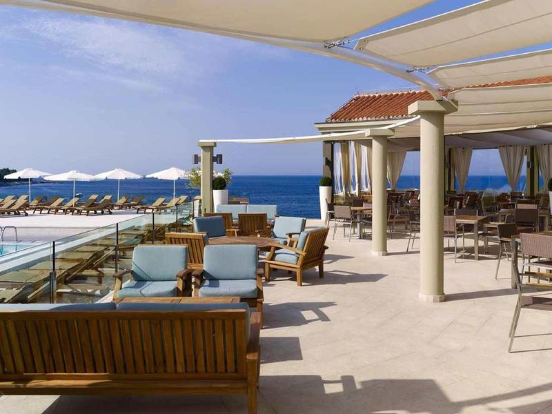 Offene Terrasse mit modernen Möbeln, weißen Sonnenschirmen und Blick auf das blaue Meer.