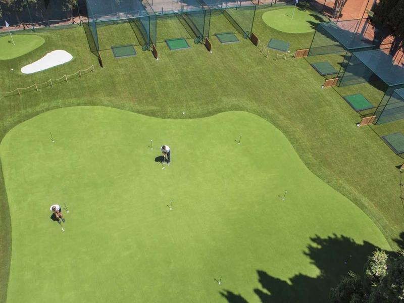 Golfplatz mit grünem Rasen, zwei Spielern, Abschlagplätzen und umgebenden Bäumen.