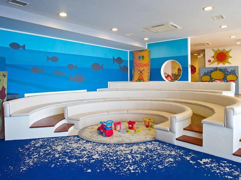 Heller, bunter Kinderspielraum mit runden weißen Sitzstufen und maritimen Wandbildern.