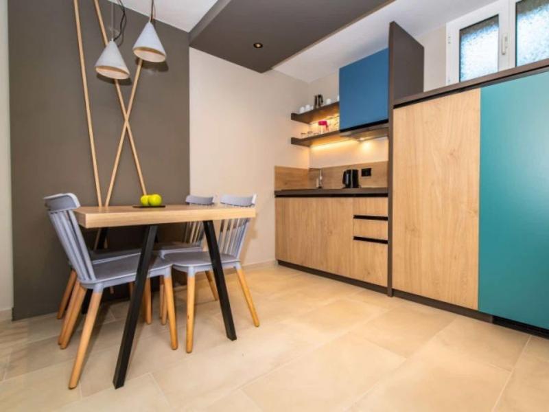 Moderner Küchenbereich mit Holzfronten, blauen Elementen, grauem Stuhl und hängenden Lampen.