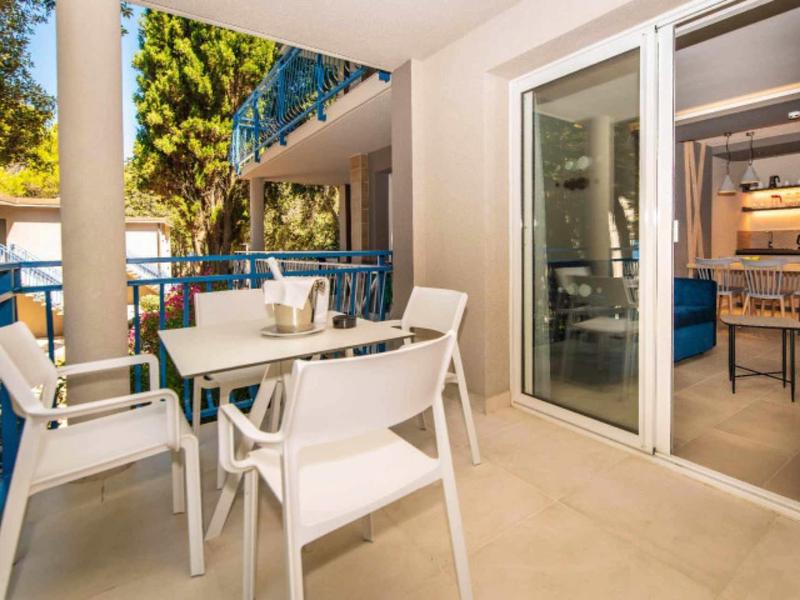 Balkon mit weißen Stühlen und Tisch, blauer Geländer, Grün und Blick ins Wohnzimmer mit Kamin.