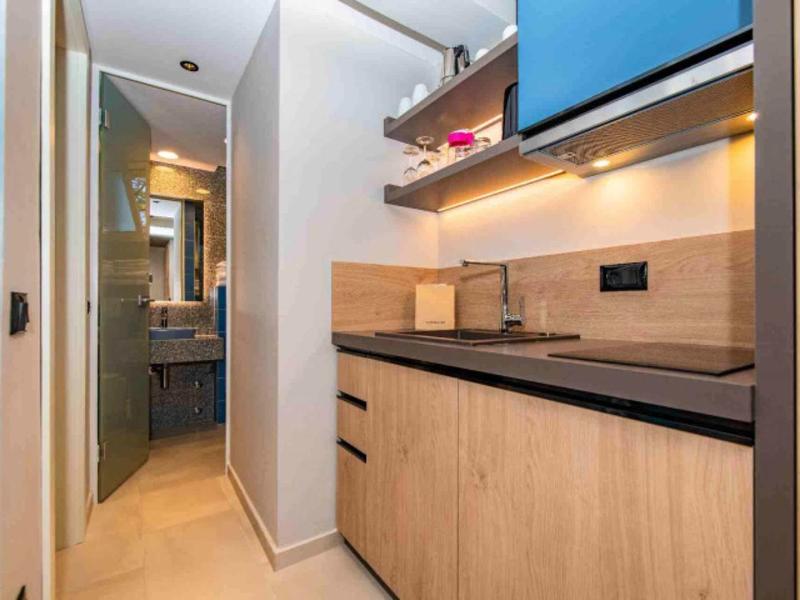 Kleine Küche mit Holzfronten, schwarzen Griffen, Arbeitsfläche und blauem Oberschrank.