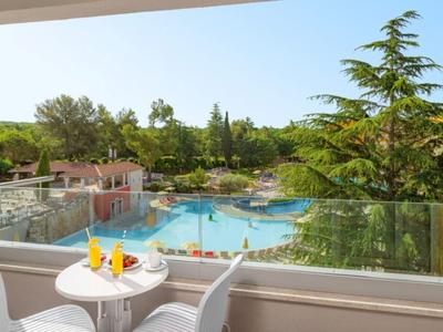 Výhled z terasy na bazén a zelené stromy pod jasnou oblohou.