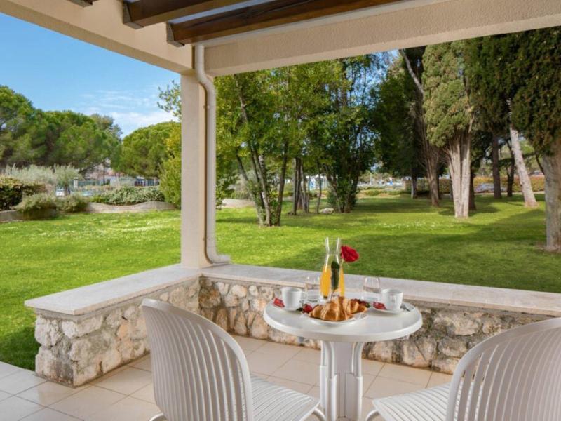 Pohodlná terasa se stolem a židlemi na zahradě s stromy a trávníkem