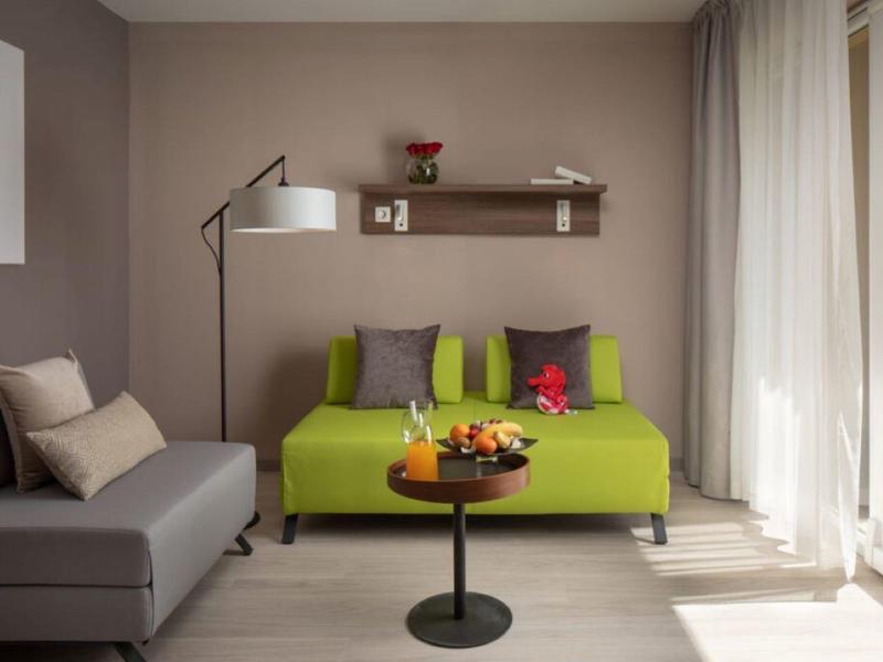 Moderní obývací pokoj se zelenou pohovkou, šedou sedačkou a velkým oknem.