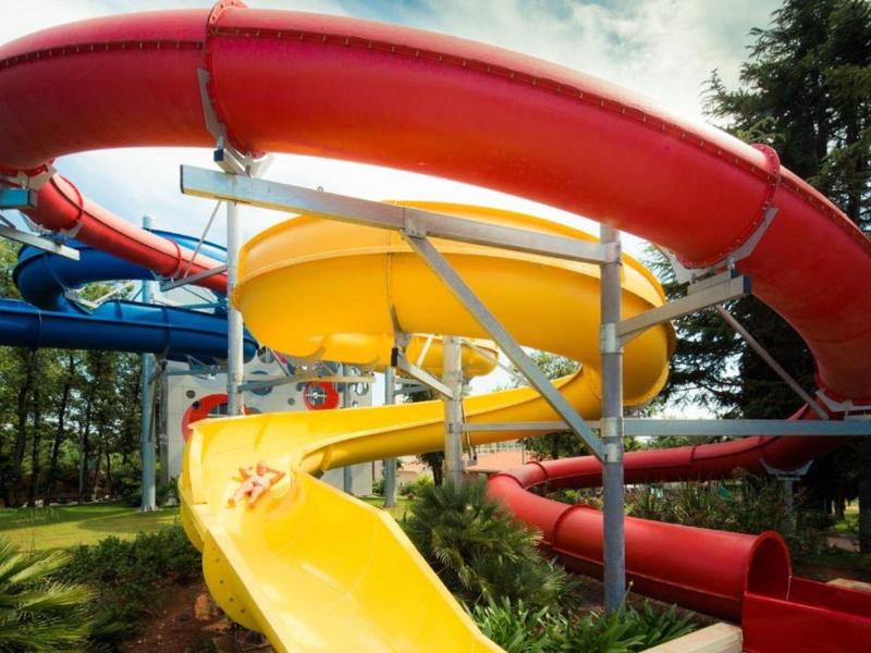 Barevné vodní skluzavky v zábavním parku obklopené stromy.